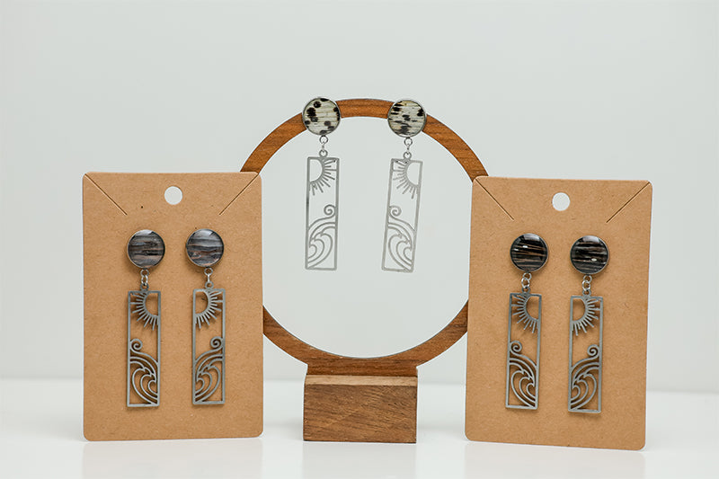 Three pairs of Surf + Shine Earrings on stands on a white background. 