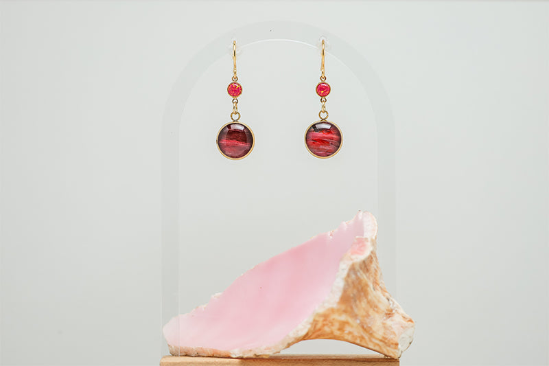 Red Flame Opal Earrings on a white background with a pink shell at the bottom of the image. 