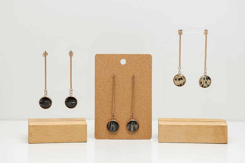 Three pairs of Long Rose Gold Drop Earrings on stands on a white background.  