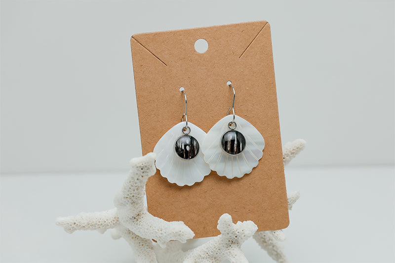 A pair of Iridescent Mother of Pearl Dangles on a cardboard stand on white coral on a white background. 