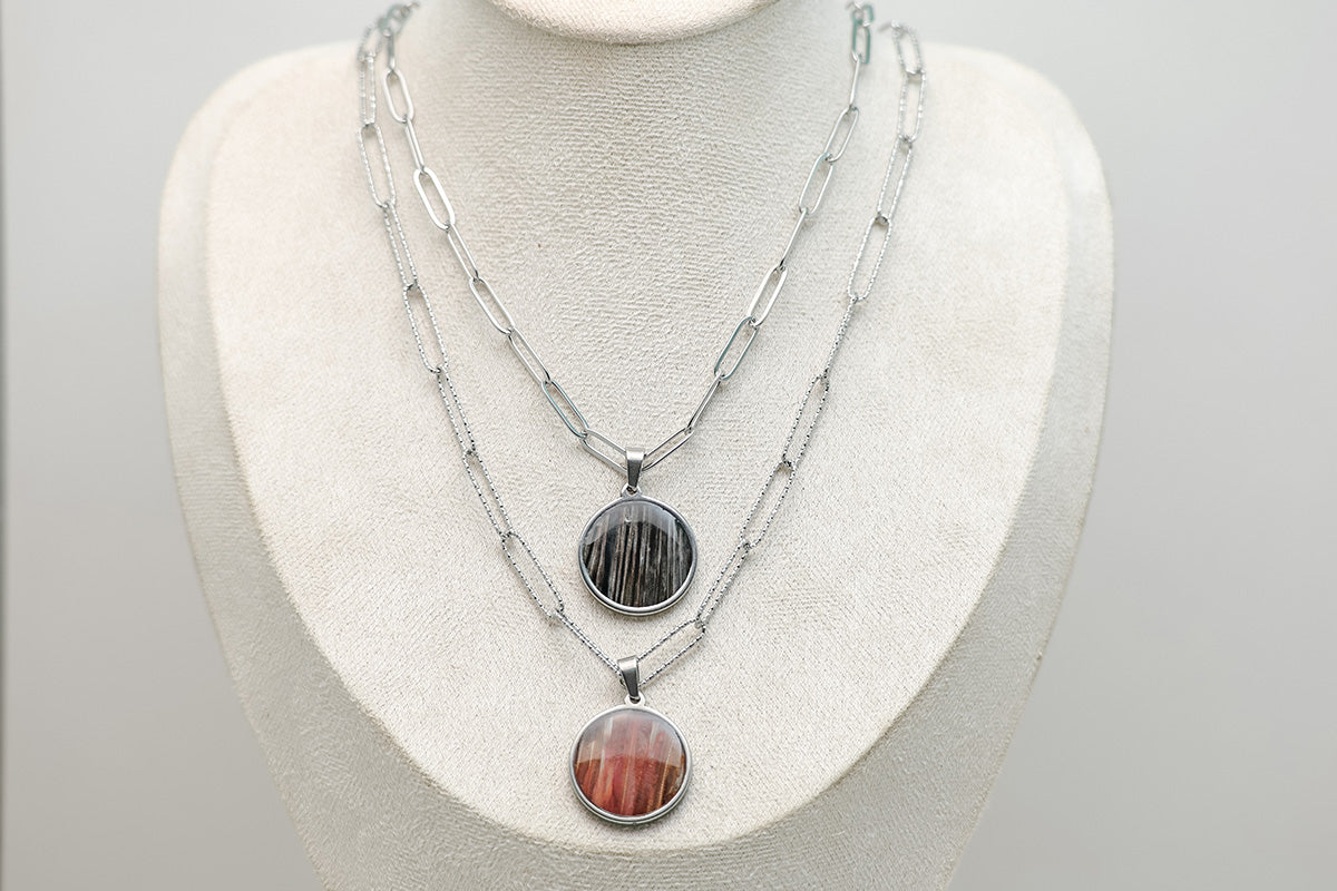 Two Large Silver Necklaces on a cream necklace display bust. 