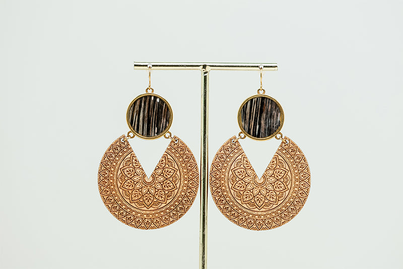 Wooden Mandala Statement Earrings dangle from a gold rod stand on a white background. 