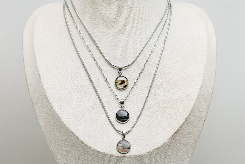 Three Small Silver Necklaces on a cream necklace display bust. 