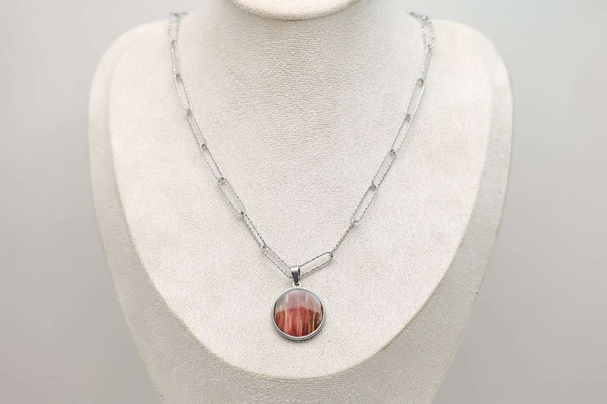 A Large Silver Necklace on a cream necklace display bust. 