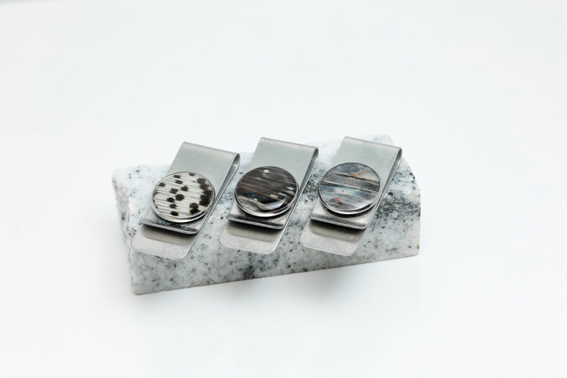 Three Money Clips on a piece of black and white marble on a white background. 