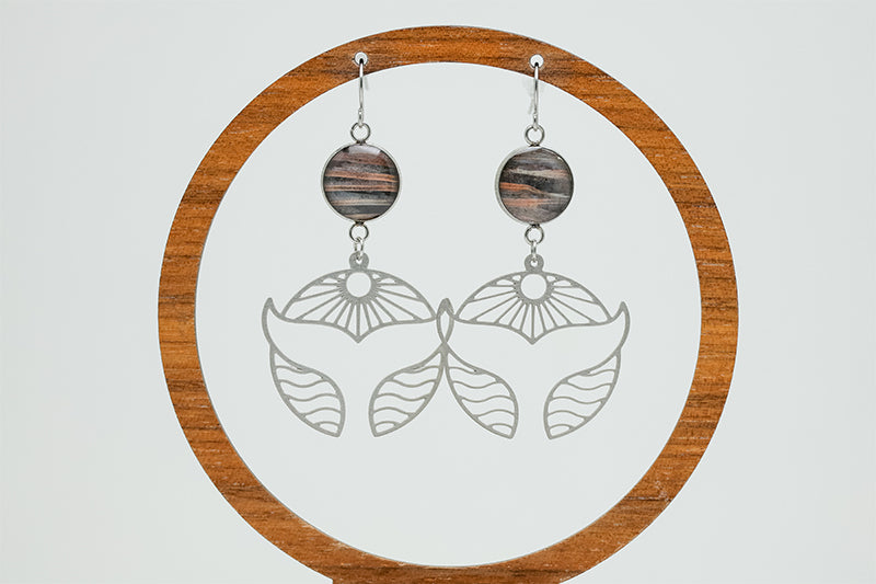 Silver Whale Tail Earrings on a circular wooden stand on a white background. 