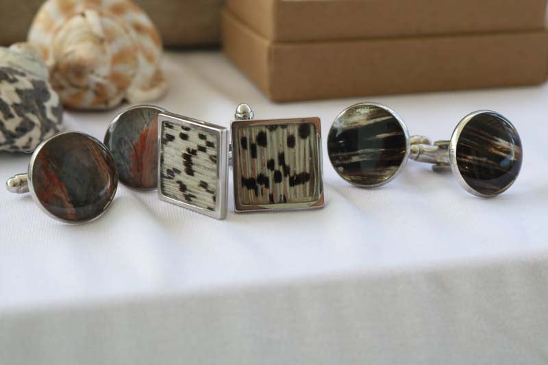 Two Round and one Square Cuff Link Sets on a white tablecloth with two shells and a jewelry box in the background.