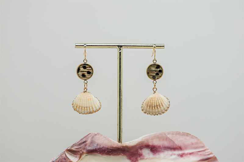 Small Scallop Shell Drops on a gold stand on a white background with a pink clam shell at the bottom of the image.