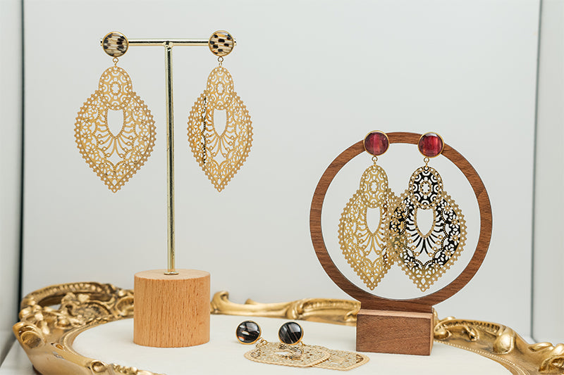 Three pairs of Golden Hour Lace Earrings on stands on a white background with a gold frame. 