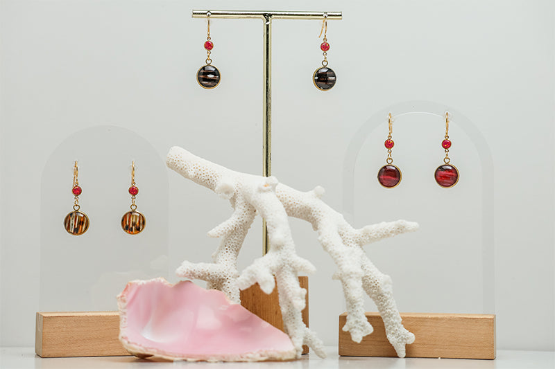 Three Red Flame Opal Earring pairs on a white background with a pink shell and a white coral at the bottom of the image. 