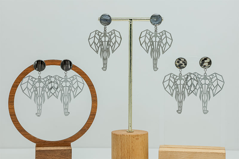 Three pairs of Geometric Elephant Earrings on stands on a white background.  