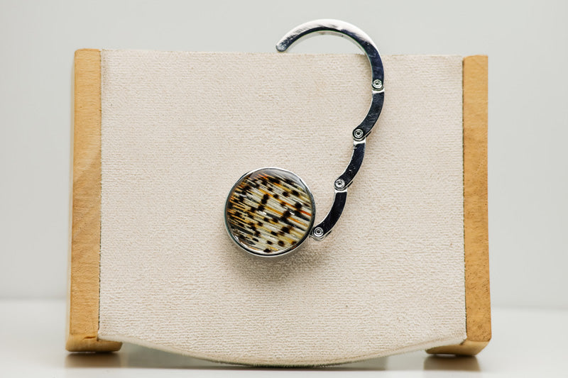 An open Silver Purse Hook Hanger on a cream block.