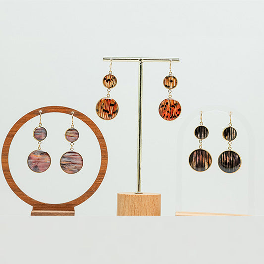 Three gold dual dangle lionfish earrings displayed on stands against a light gray background