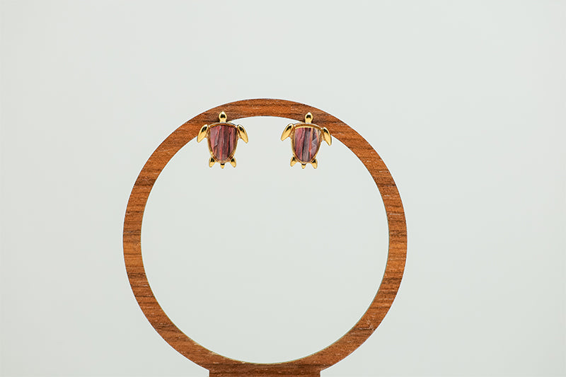 Mini Gold Turtle earrings on a circular wooden stand on a white background.  