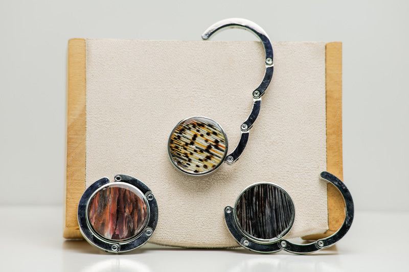 Three silver Purse Hook Hangers on a cream block, one is open, one is half open and one is closed. 